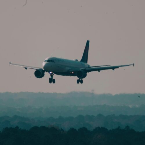 A large Delta Air Lines passenger jet performing a controlled landing on a runway, with emergency fire trucks and ground crew vehicles stationed nearby with flashing lights to ensure passenger safety.