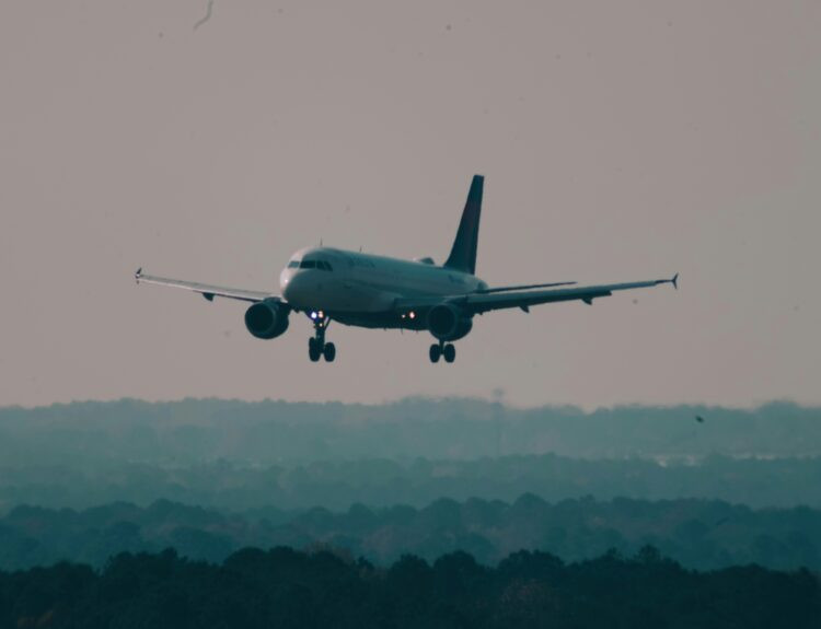 A large Delta Air Lines passenger jet performing a controlled landing on a runway, with emergency fire trucks and ground crew vehicles stationed nearby with flashing lights to ensure passenger safety.