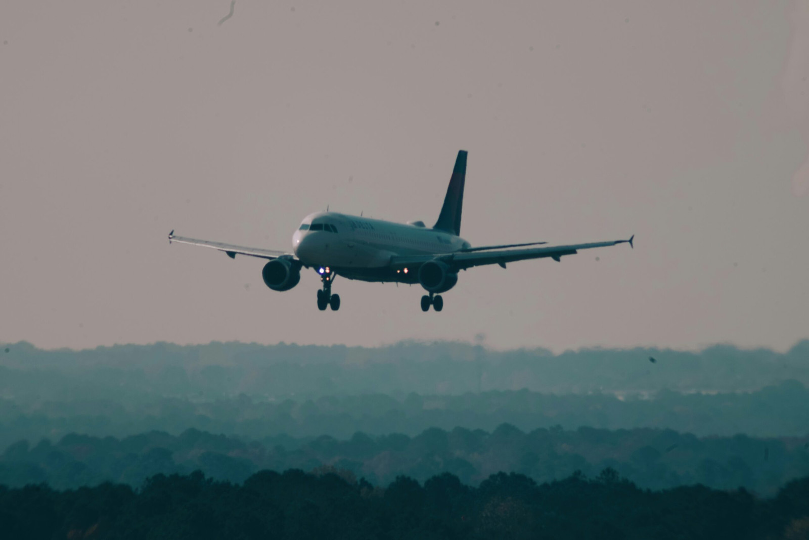 A large Delta Air Lines passenger jet performing a controlled landing on a runway, with emergency fire trucks and ground crew vehicles stationed nearby with flashing lights to ensure passenger safety.